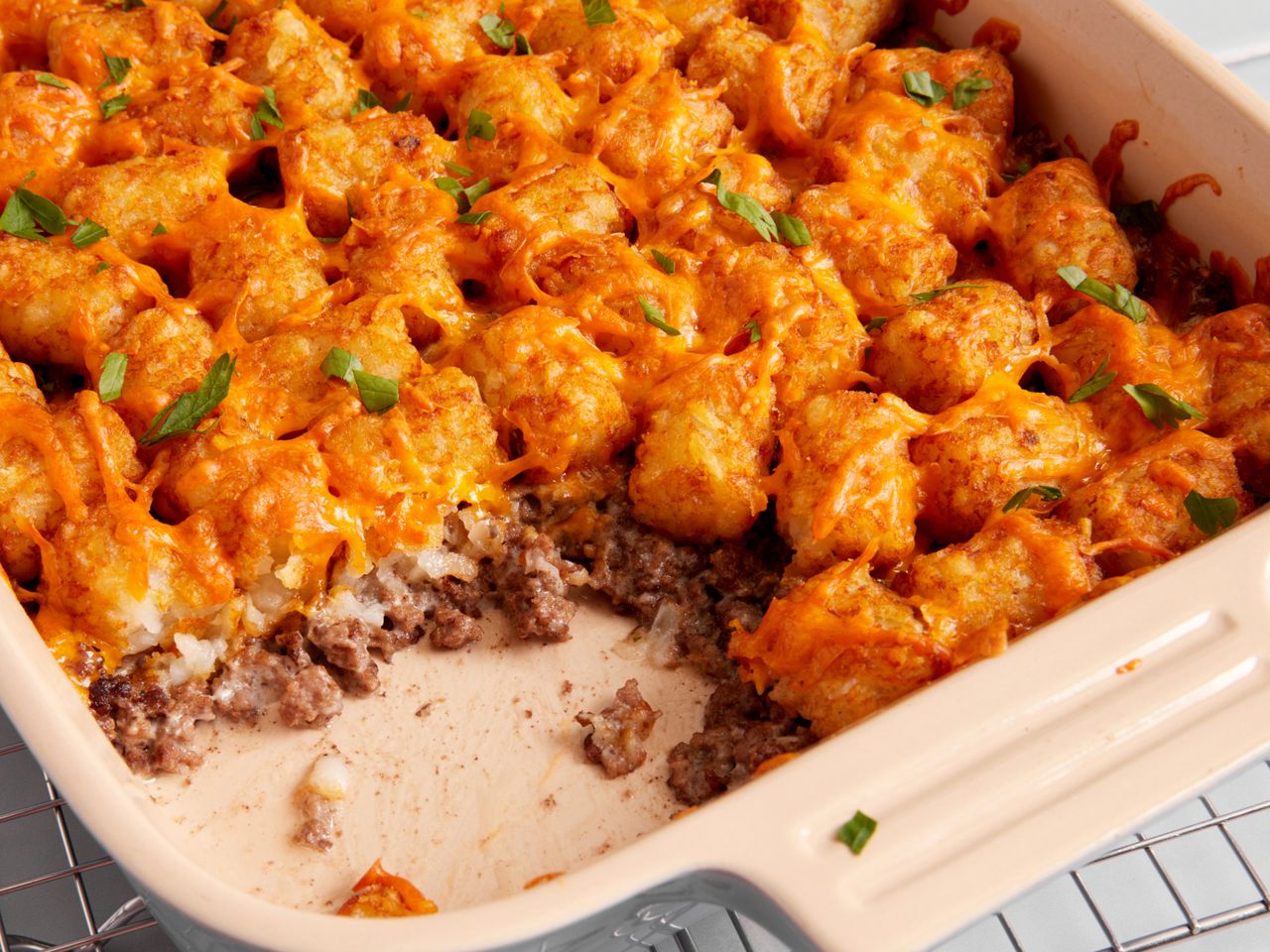 closeup of cheddar-topped Tater Tot Casserole in a white ceramic baking dish with a serving scooped out of it