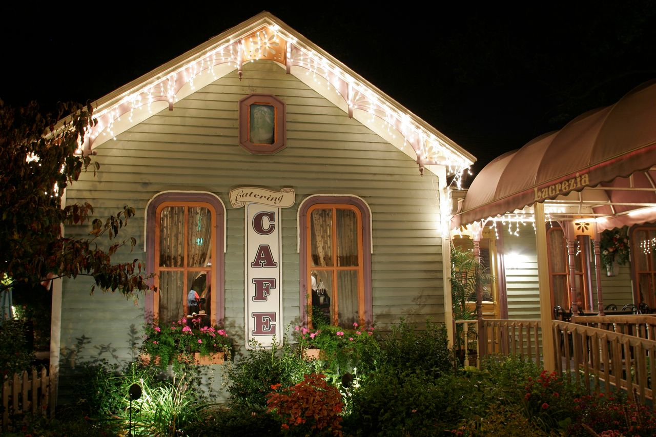 A small welllit caf exterior at night illuminated by string lights surrounded by plants and a wooden fence
