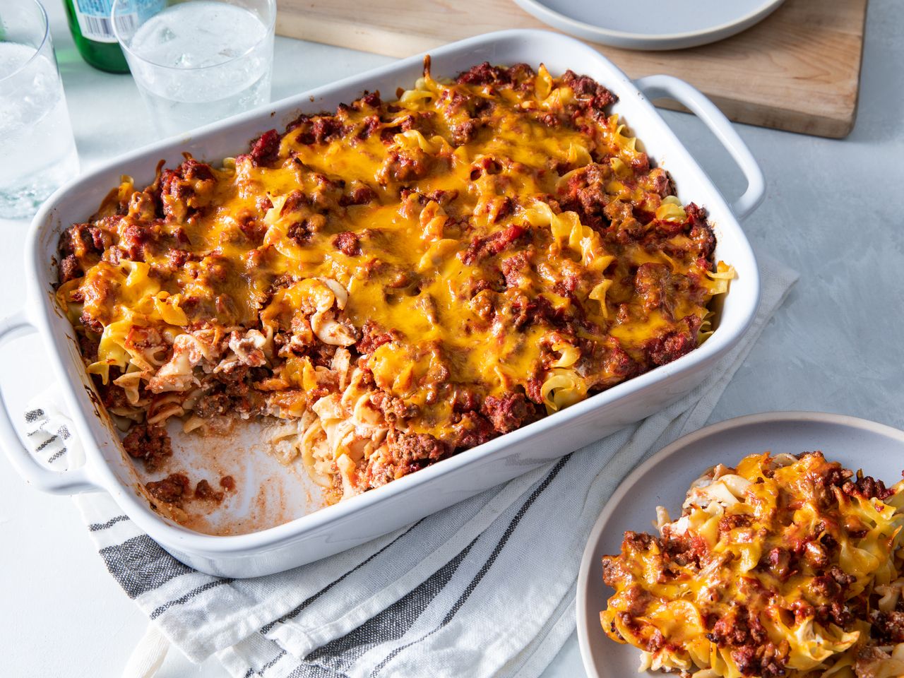 cheesy beef and pasta casserole in a white casserole dish with a portion taken out on a separate plate.