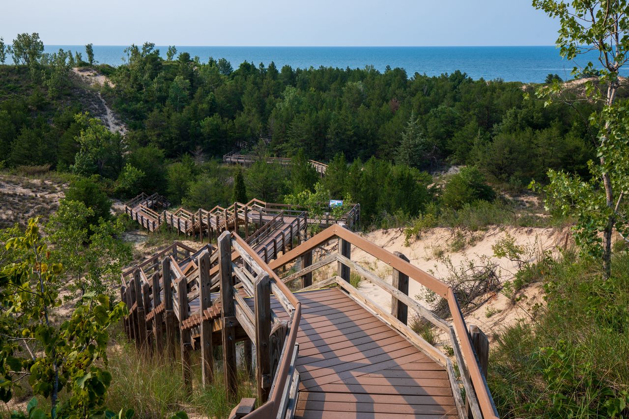 Wooden stairs leading through a sandy area with trees to Lake Michigan