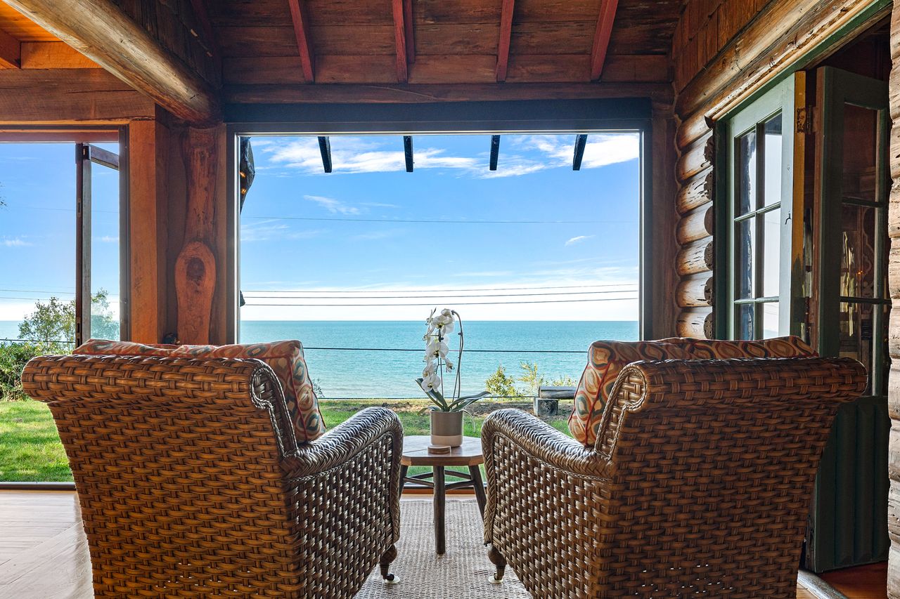 Two wicker chairs facing a lake located in a wooden cabinstyle room with large open windows