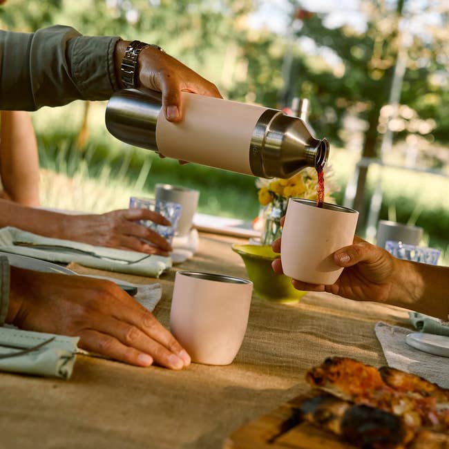 Pouring drink from a steel thermos into metal cups on an outdoor table