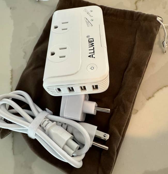 The voltage converter with dual outlets and several USB ports, placed on a drawstring pouch