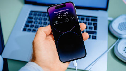Close up of an iPhone with a MacBook in the background.