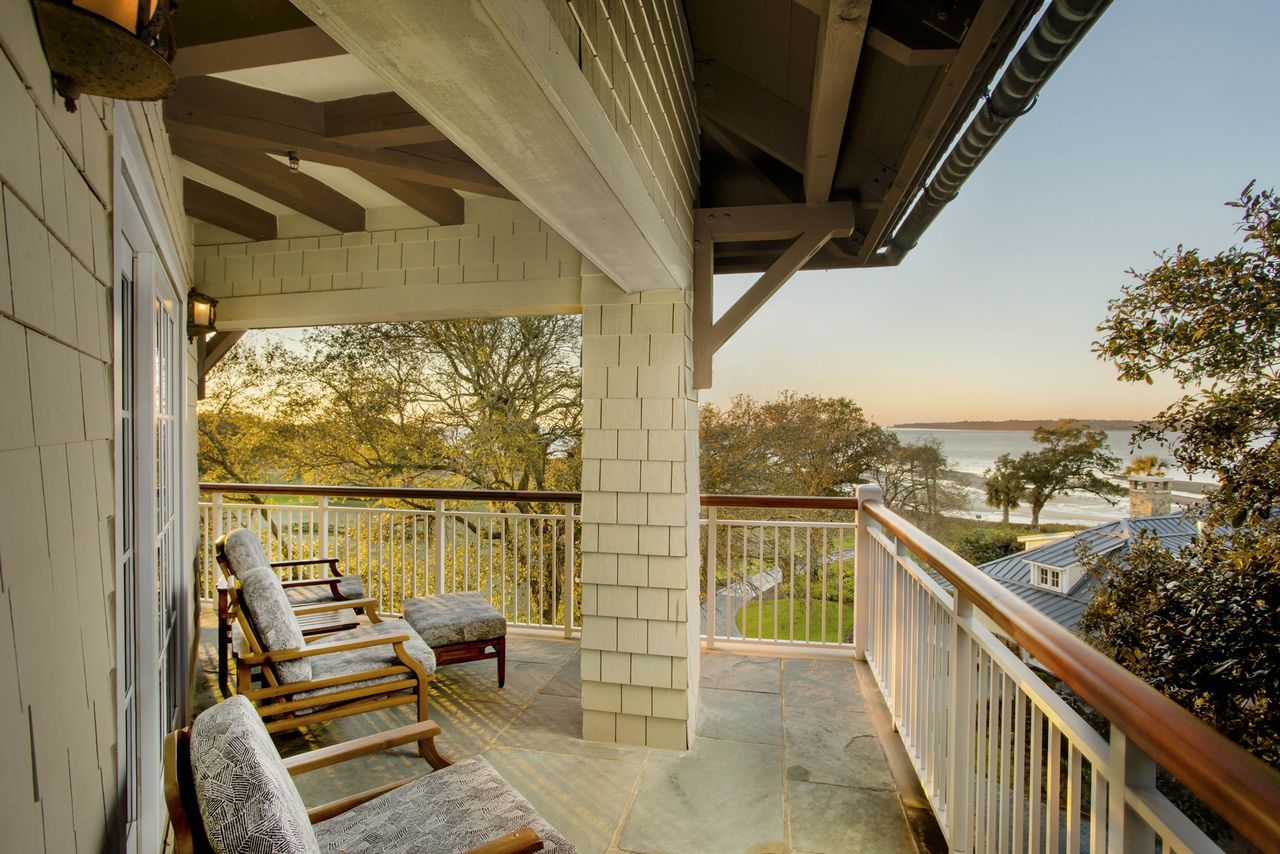 Outdoor seating area on a wooden balcony overlooking a scenic waterfront landscape with trees and distant buildings