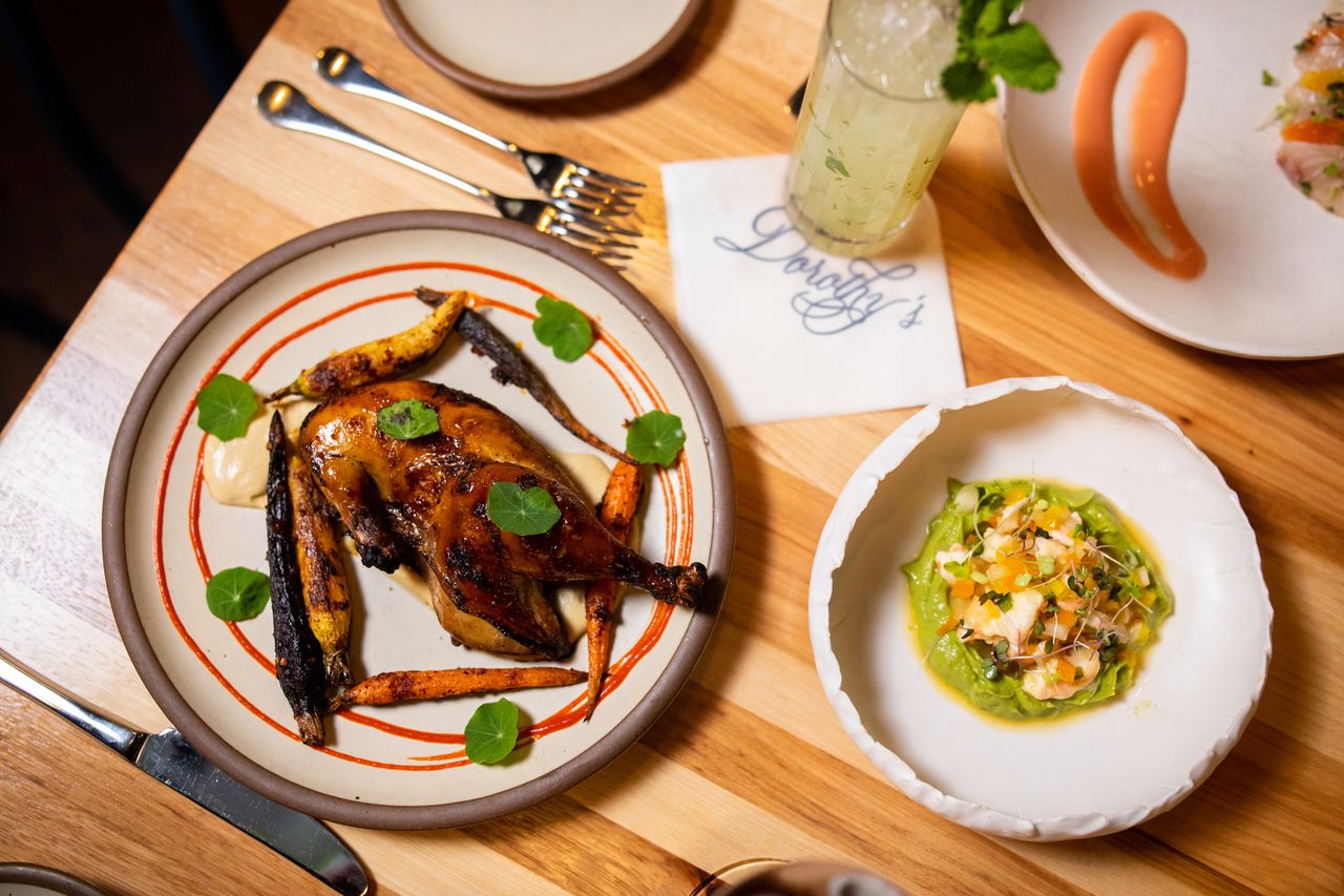 A food dish with roasted chicken and carrots alongside a plated appetizer on a wooden table