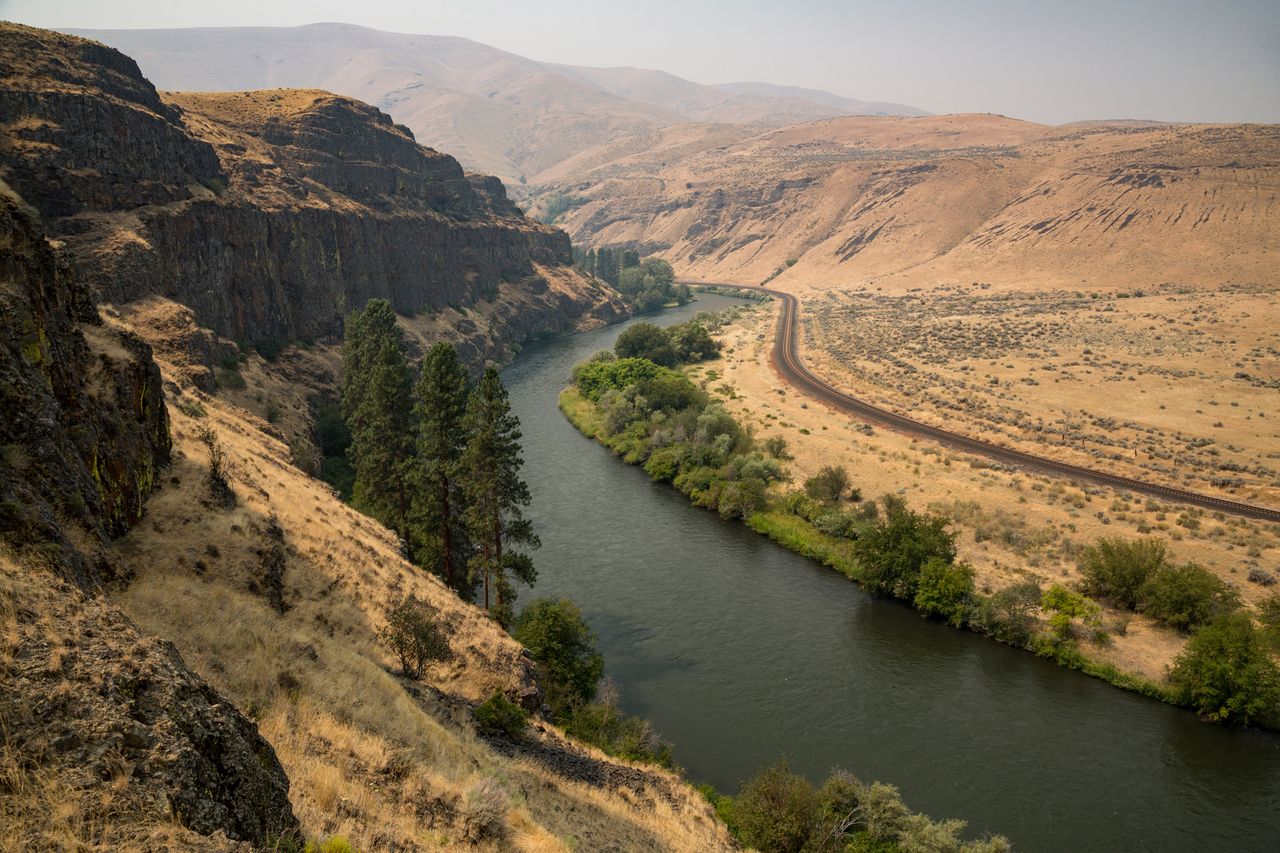 A river winding through a canyon with hills and sparse vegetation a railway track runs alongside