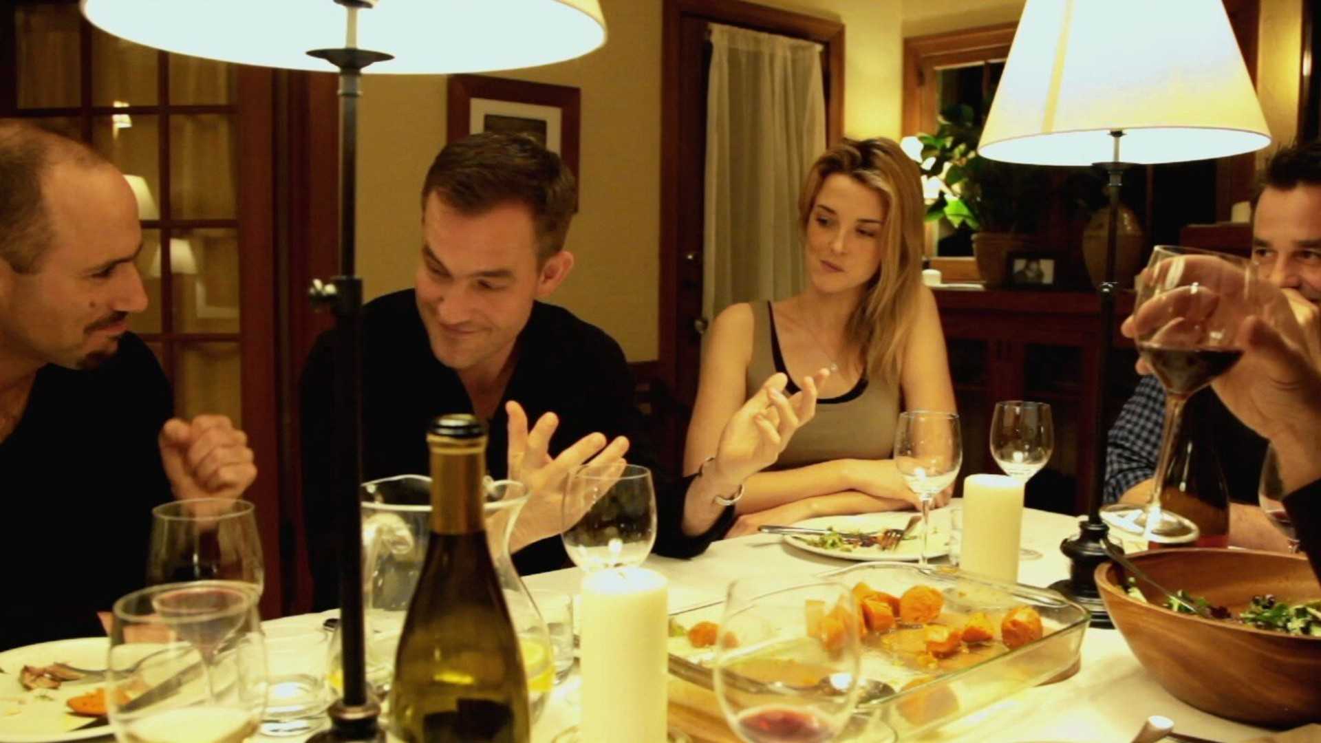 Friends laugh and talk while sitting at the dinner table in Coherence