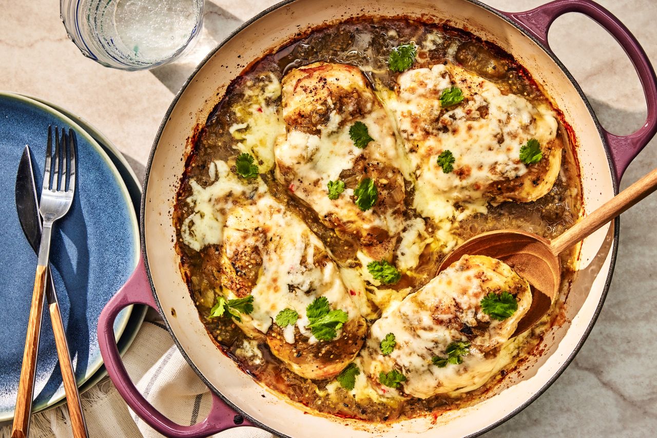 salsa verde chicken in a dutch oven at a table setting with a stack of plates with utensils and a glass of water