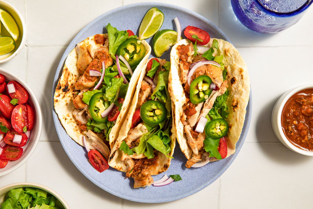 Plate of chicken tacos garnished with jalapeños, onions, and greens, served with lime wedges and salsa on the side