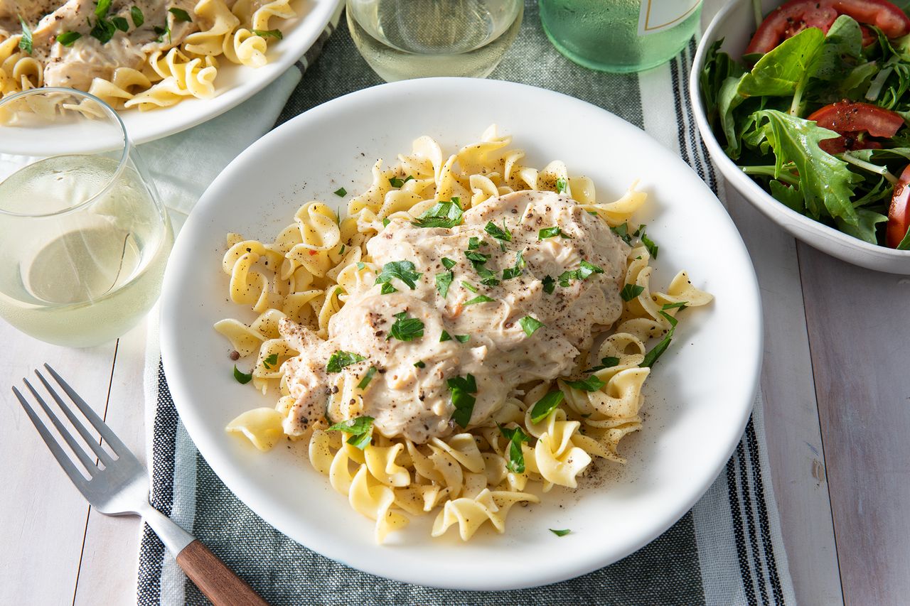Looking down on a serving of slow-cooker chicken tetrazzini served over egg noodles and garnished with fresh chopped parsley. Served with a green salad and glass of white wine.