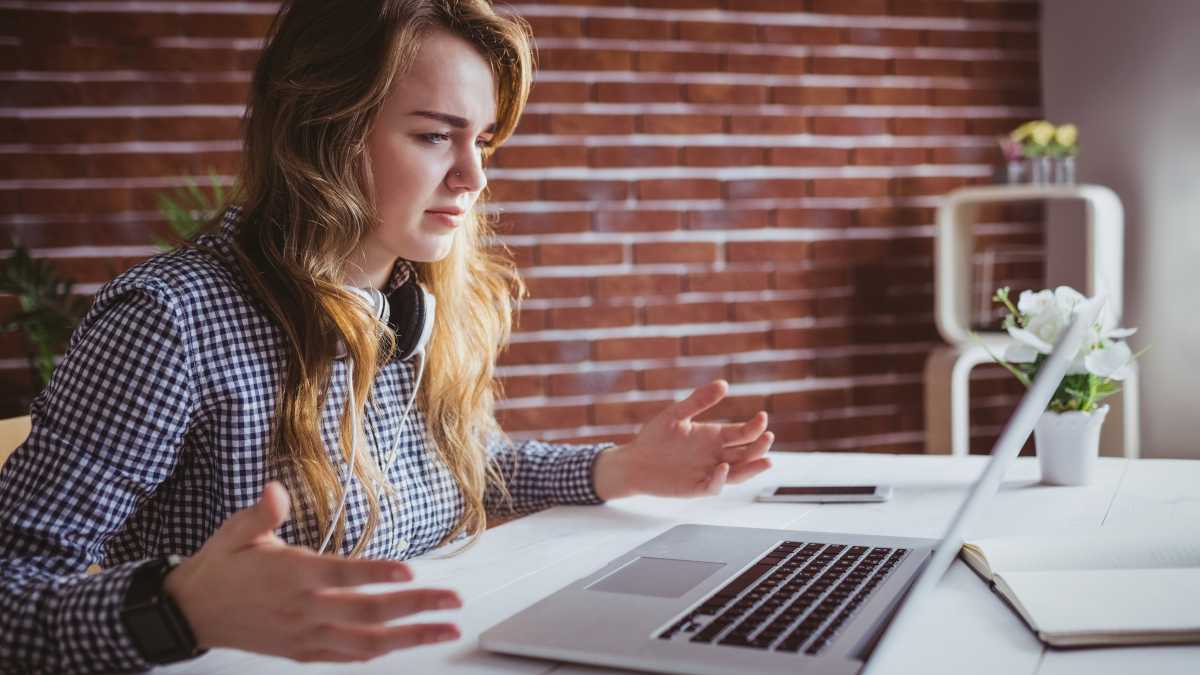 Young woman with her hands up in frustration with a Macbook laptop