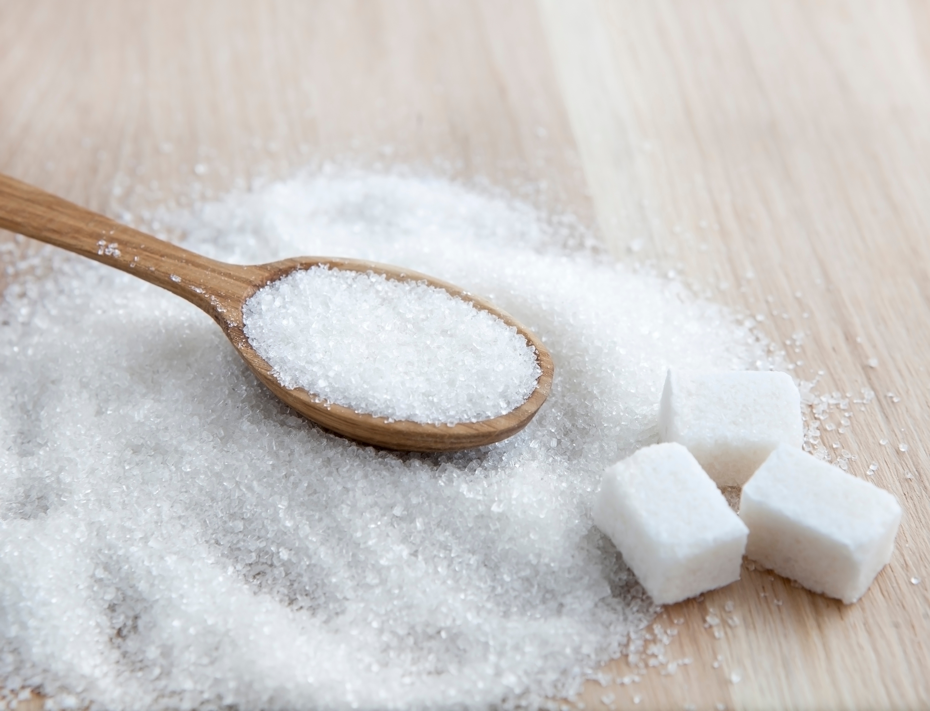 Wooden spoon with granulated sugar next to three sugar cubes on a wooden surface