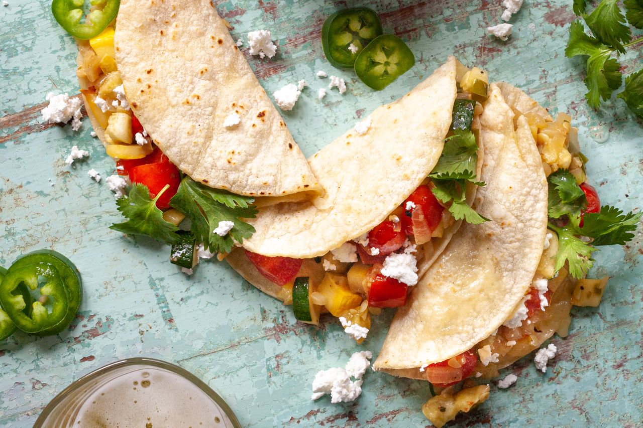 Overhead view of three vegan tacos with vegetables visible in the tacos.