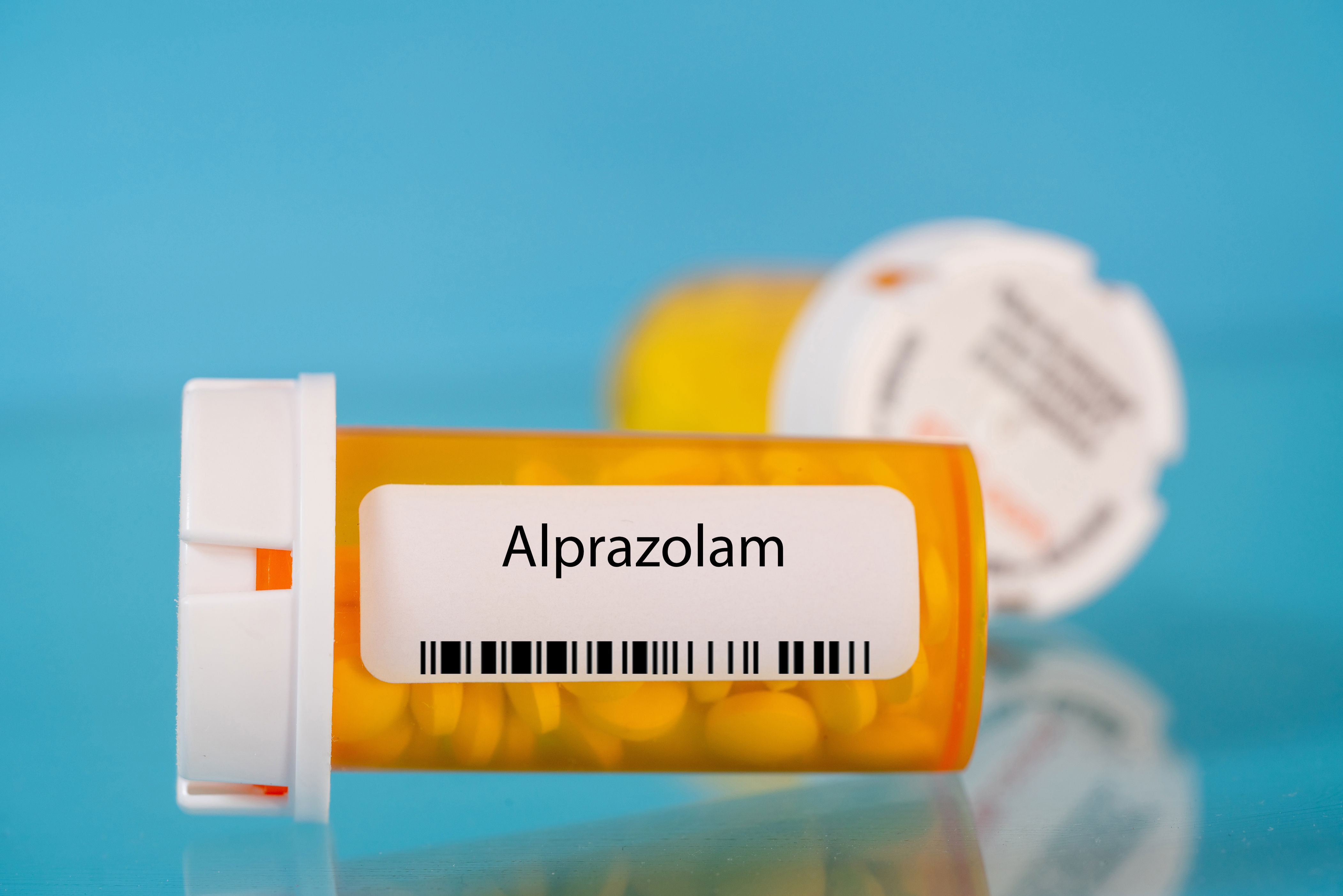 Prescription bottle labeled "Alprazolam" with pills inside, against a blue background