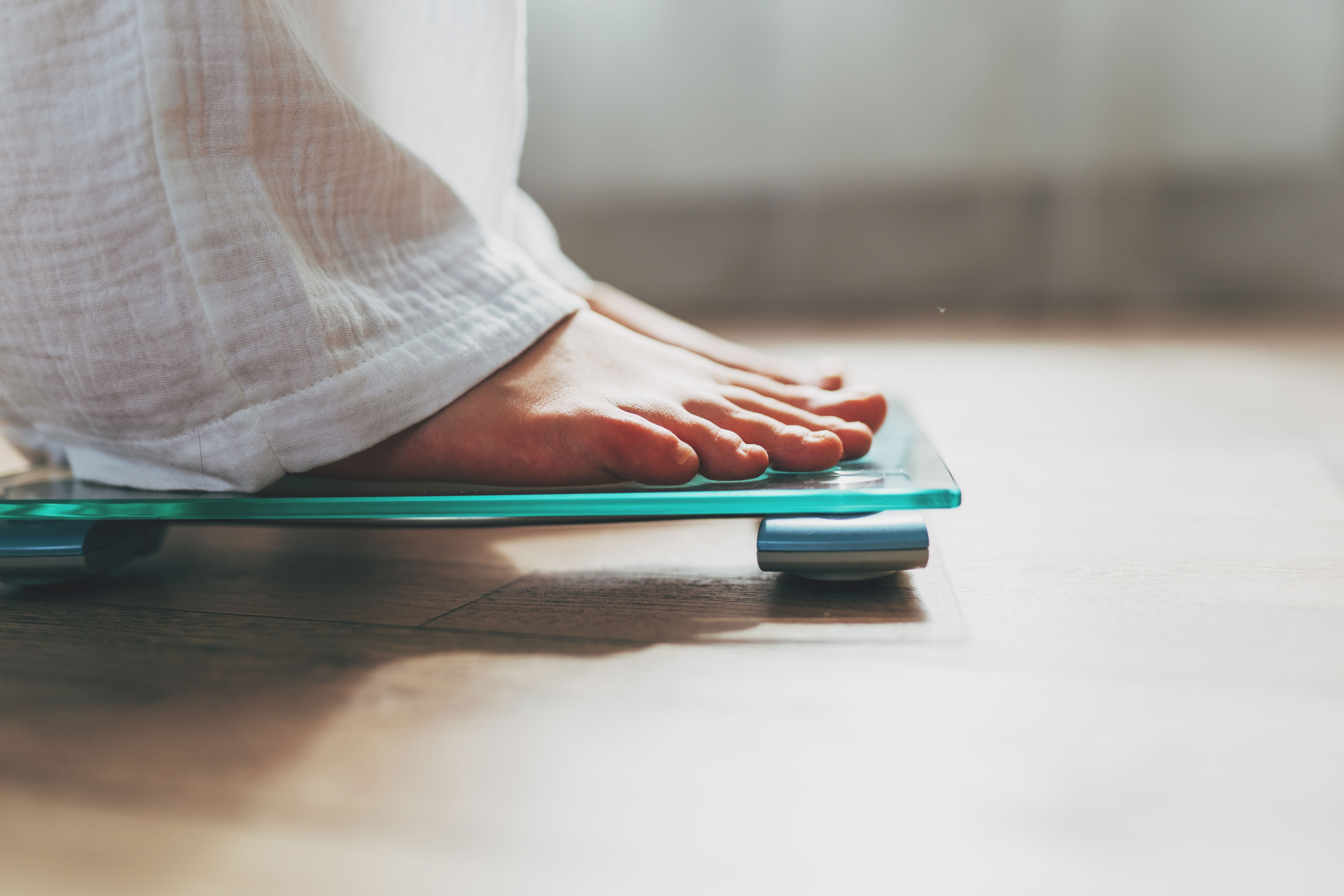 Feet on a glass bathroom scale on a wooden floor