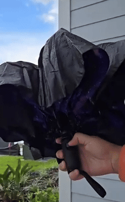 Person demonstrating a reverse-folding umbrella near a house exterior