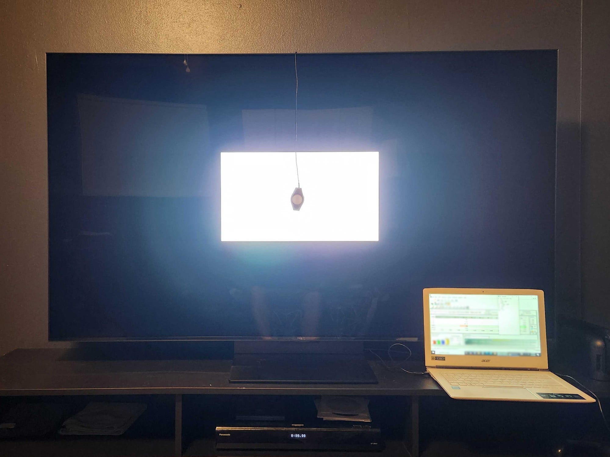 A TCL QM7K TV on a media console with a colorimeter placed on a white box displayed on the screen.
