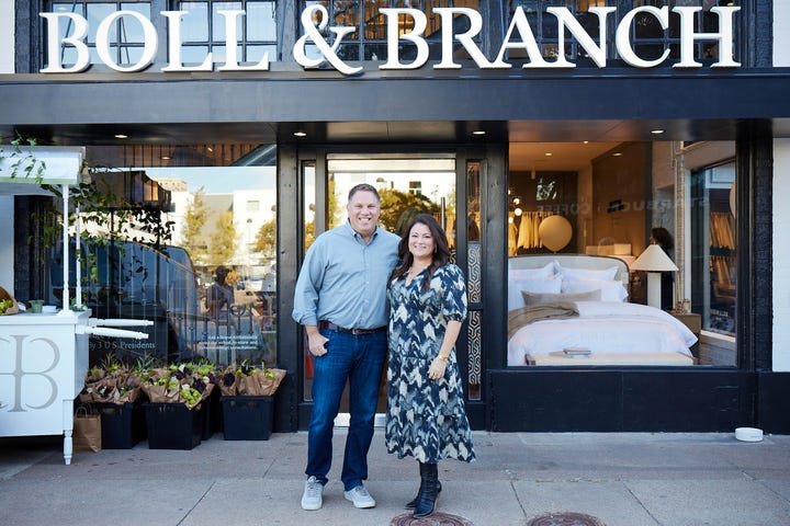 A man and woman stand in front of a retail store.