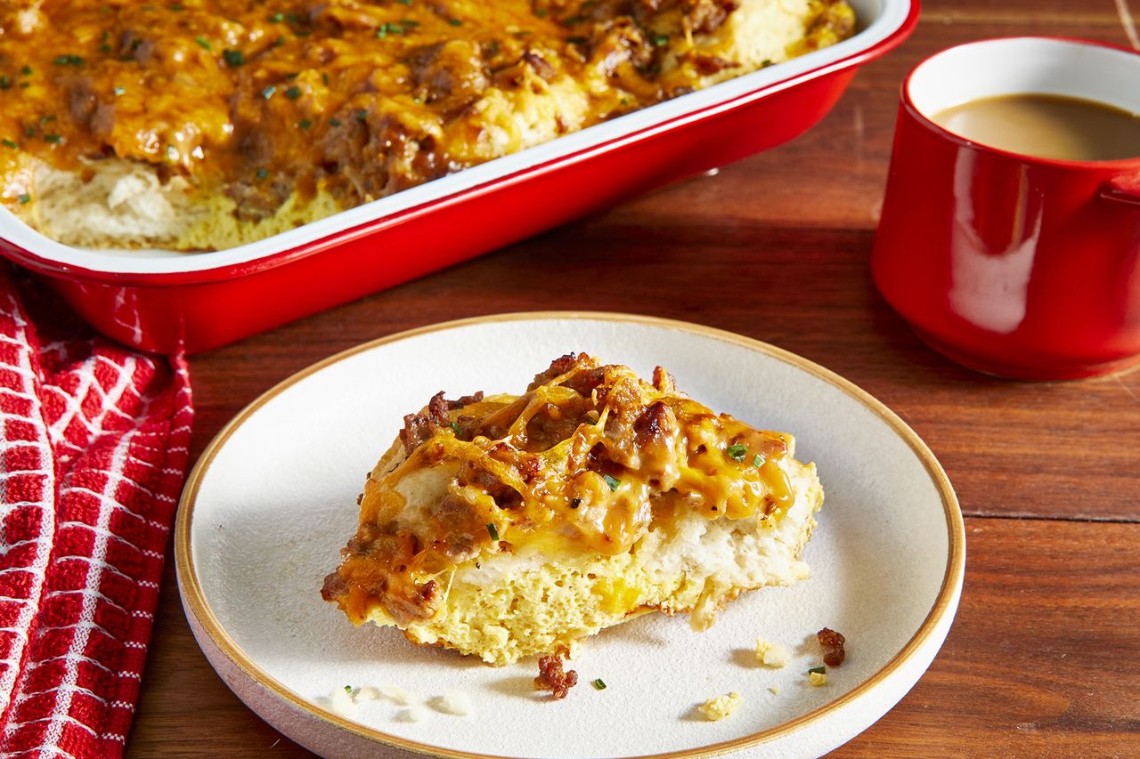 A plated piece of biscuit and gravy casserole sits in front of the red baking dish.