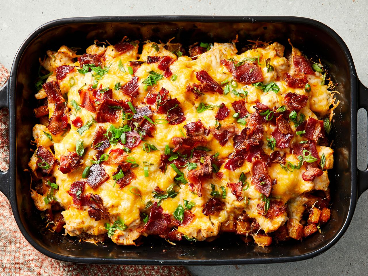 Baked casserole dish with buffalo chicken roasted potatoes bacon pieces and melted cheese topped with herbs
