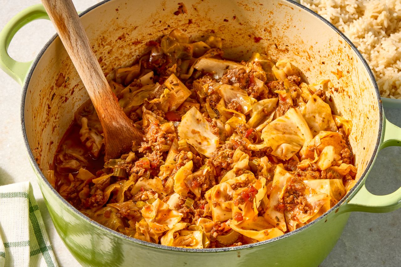 Onepot ground beef and cabbage dish being cooked in a green Dutch oven with a wooden spoon