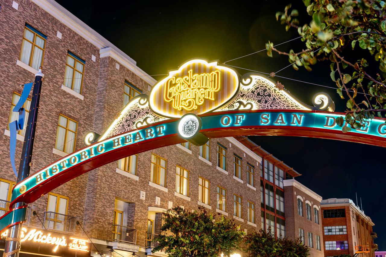 The Gaslamp Quarter archway in San Diego at nighttime surrounded by litup buildings and tree branches in the foreground