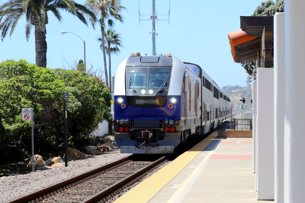 A train approaching a station platform flanked by palm trees and buildings