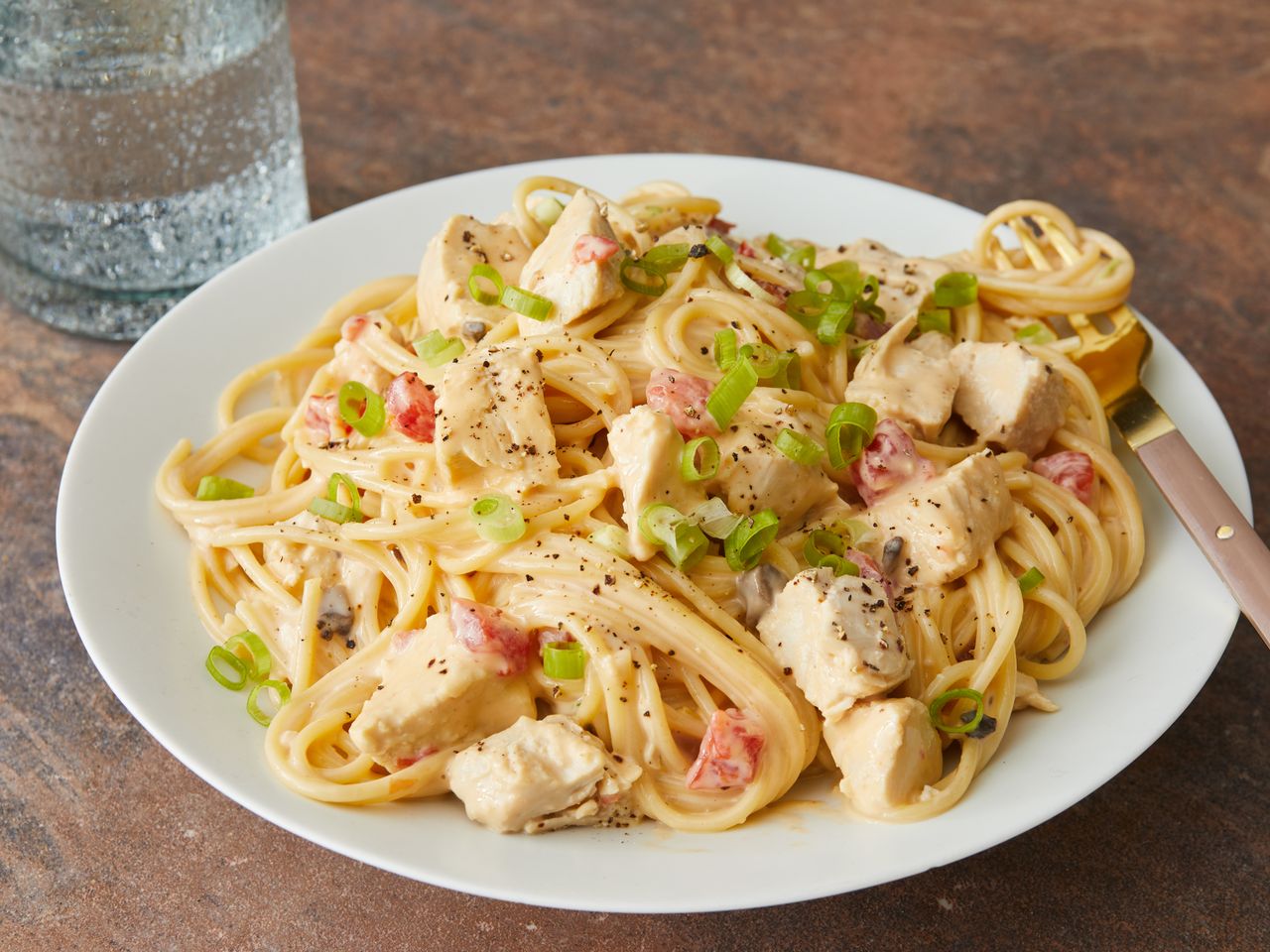Close up on a plate of chicken spaghetti garnished with green onions, with a fork