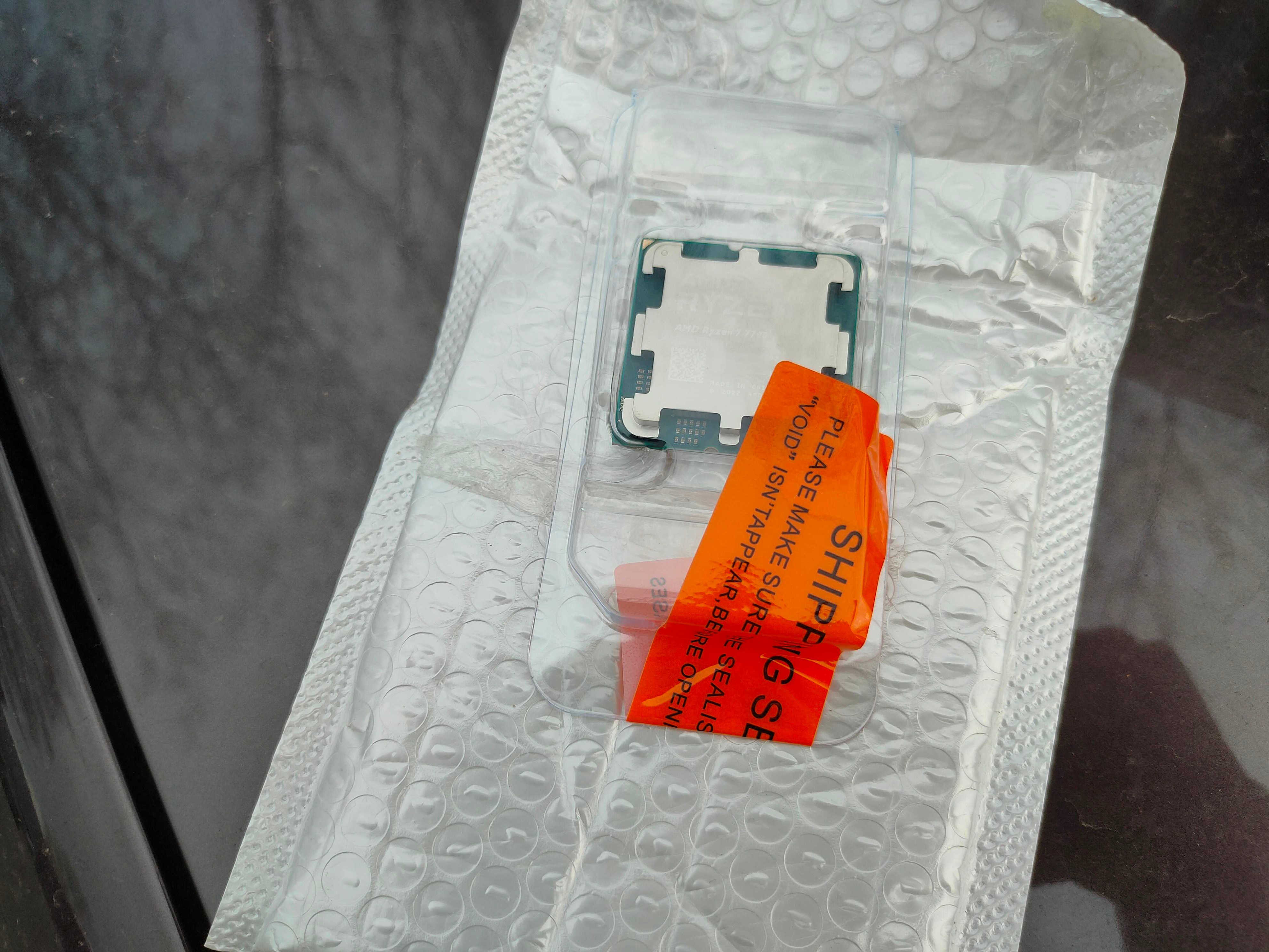 The AMD Ryzen 7 7700 CPU in a CPU tray with an orange shipping label.