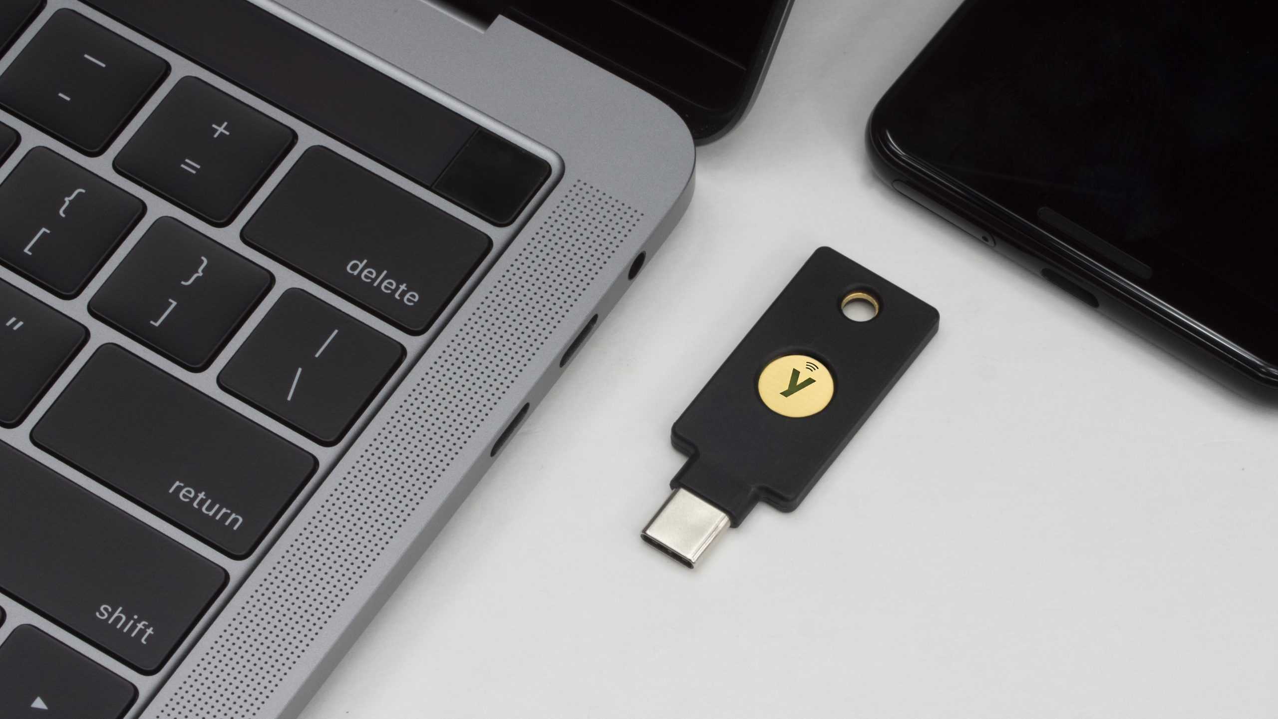 A YubiKey 5C NFC security dongle next to a MacBook and Android phone.