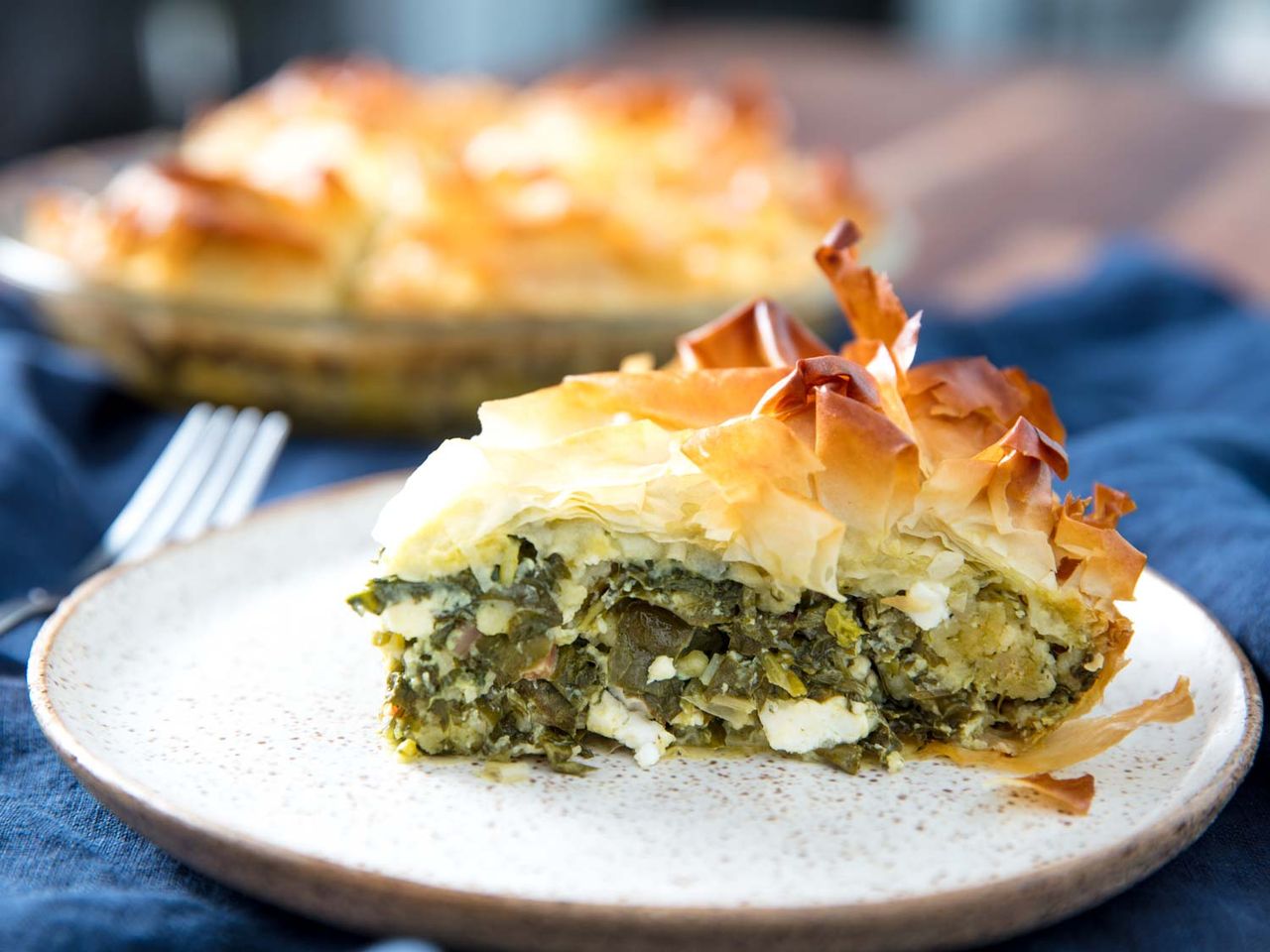 Profile closeup of a slice of spanakopita, served on a speckled ceramic plate.