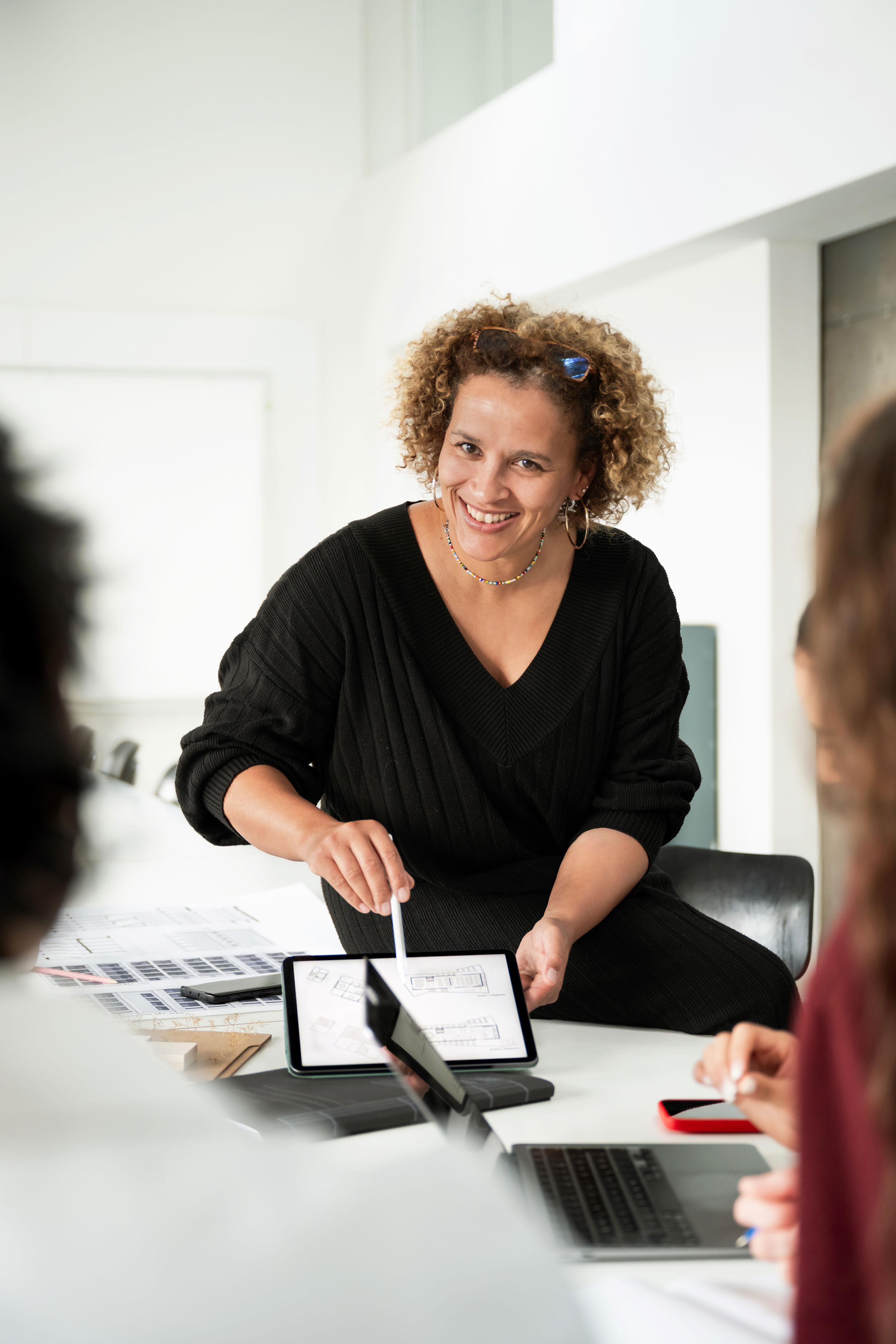 Person in a professional setting, presenting tablet to colleagues. Engaged in discussion, suggesting a collaborative work environment