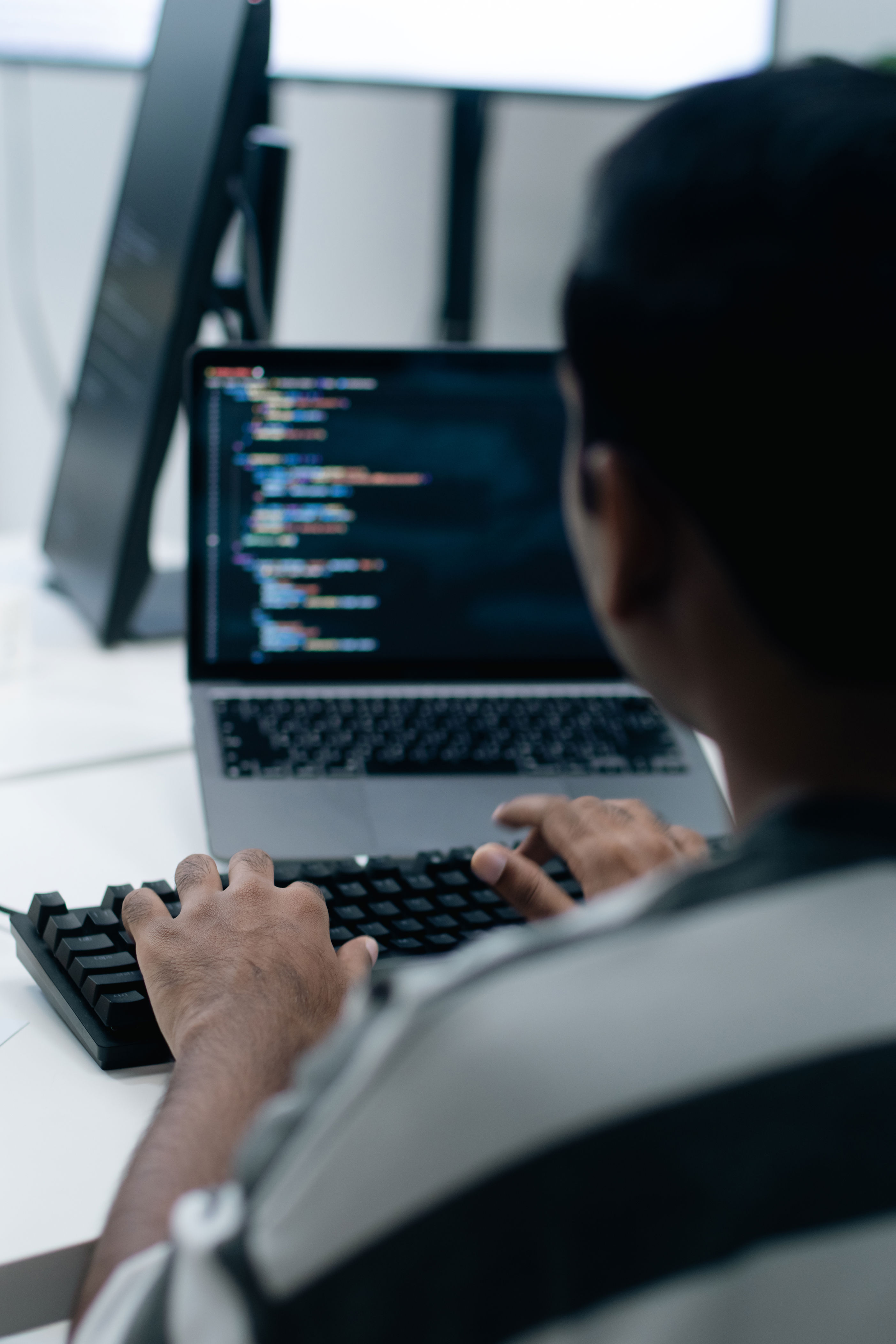 Person typing code on a laptop at a workstation, focusing on a programming task