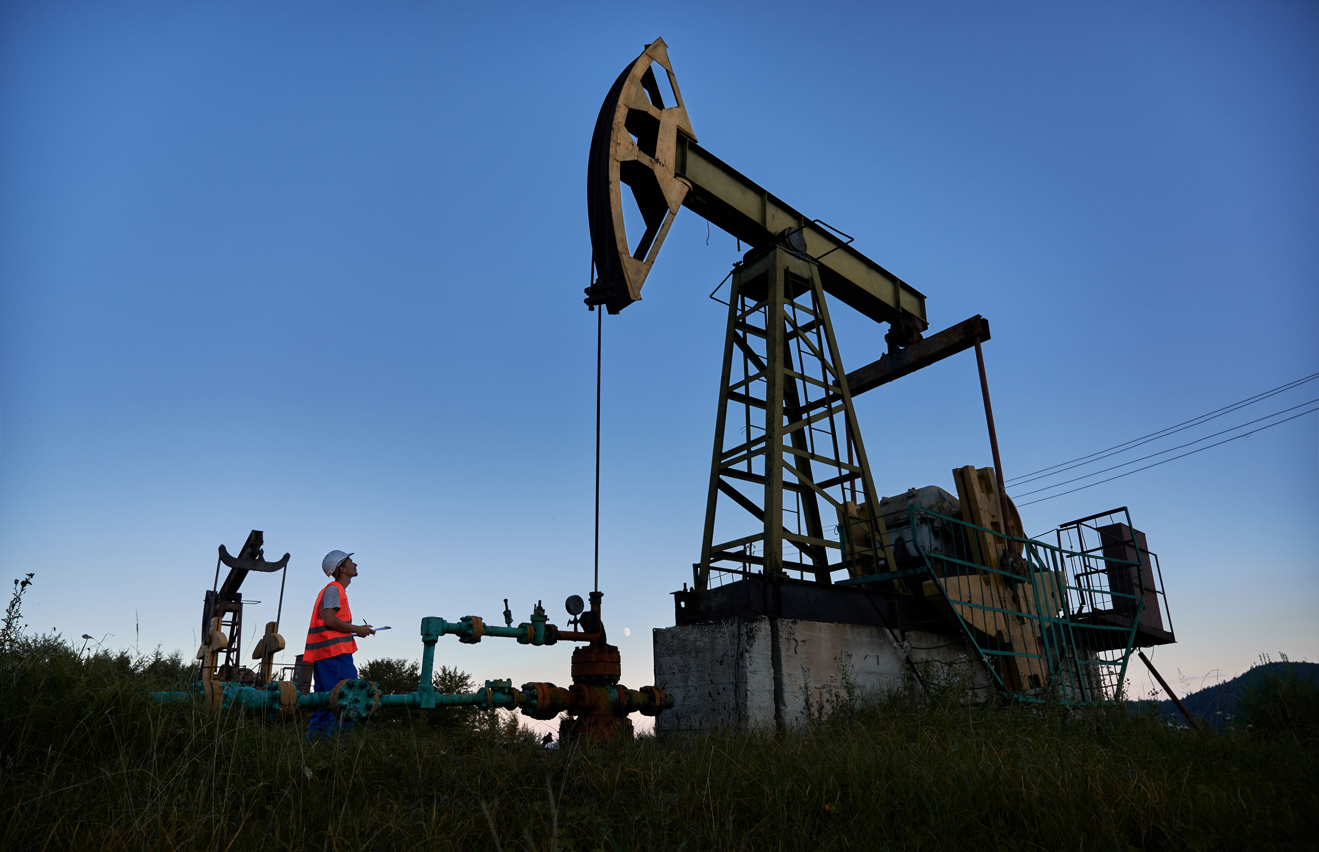 A worker inspects equipment at an oil pumpjack in a field, highlighting oil industry operations for an article on Work & Money