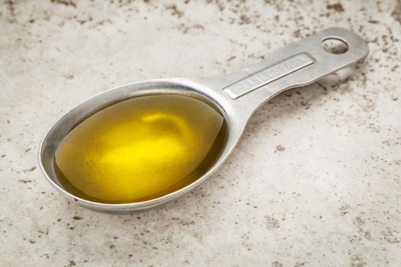 A stainless steel measuring tablespoon filled with olive oil