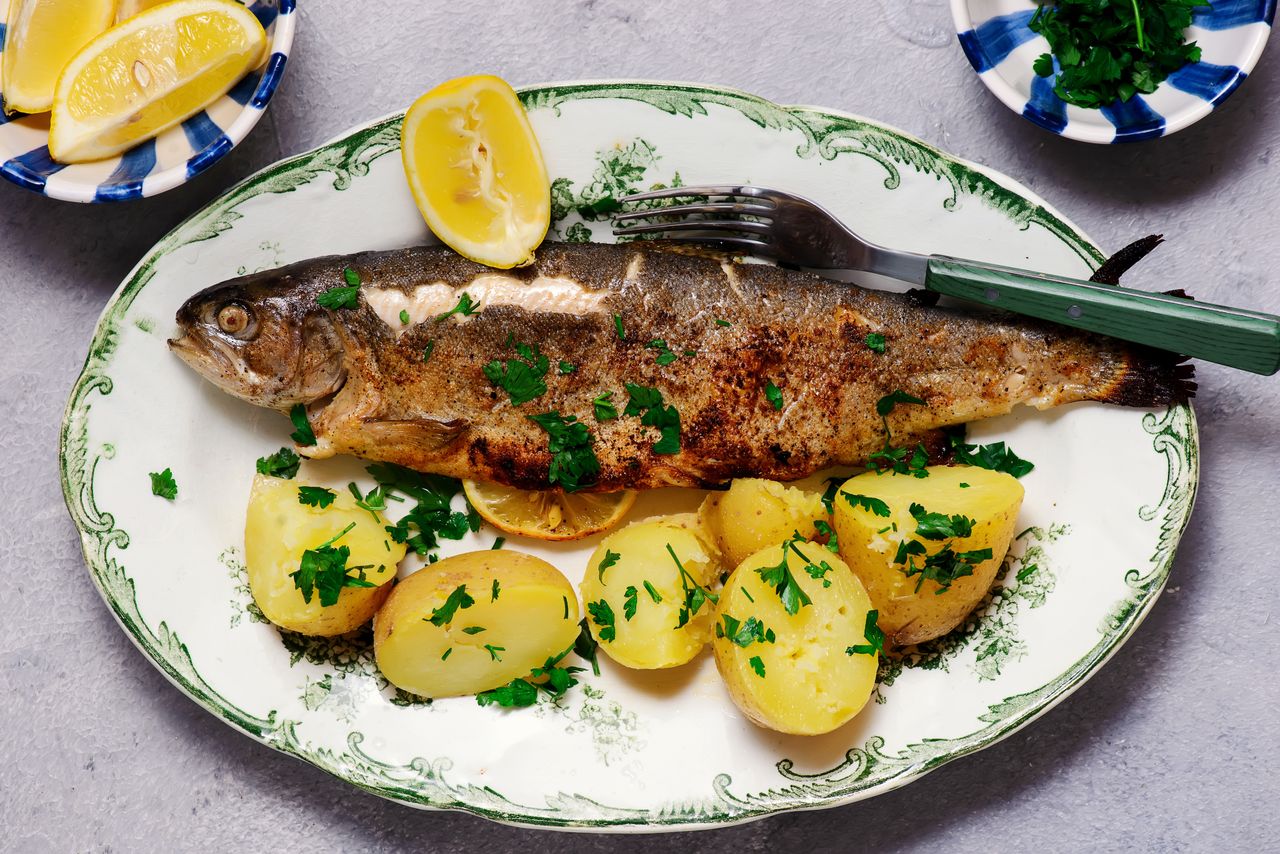 Cooked whole fish served with potatoes and garnished with herbs on a decorative plate