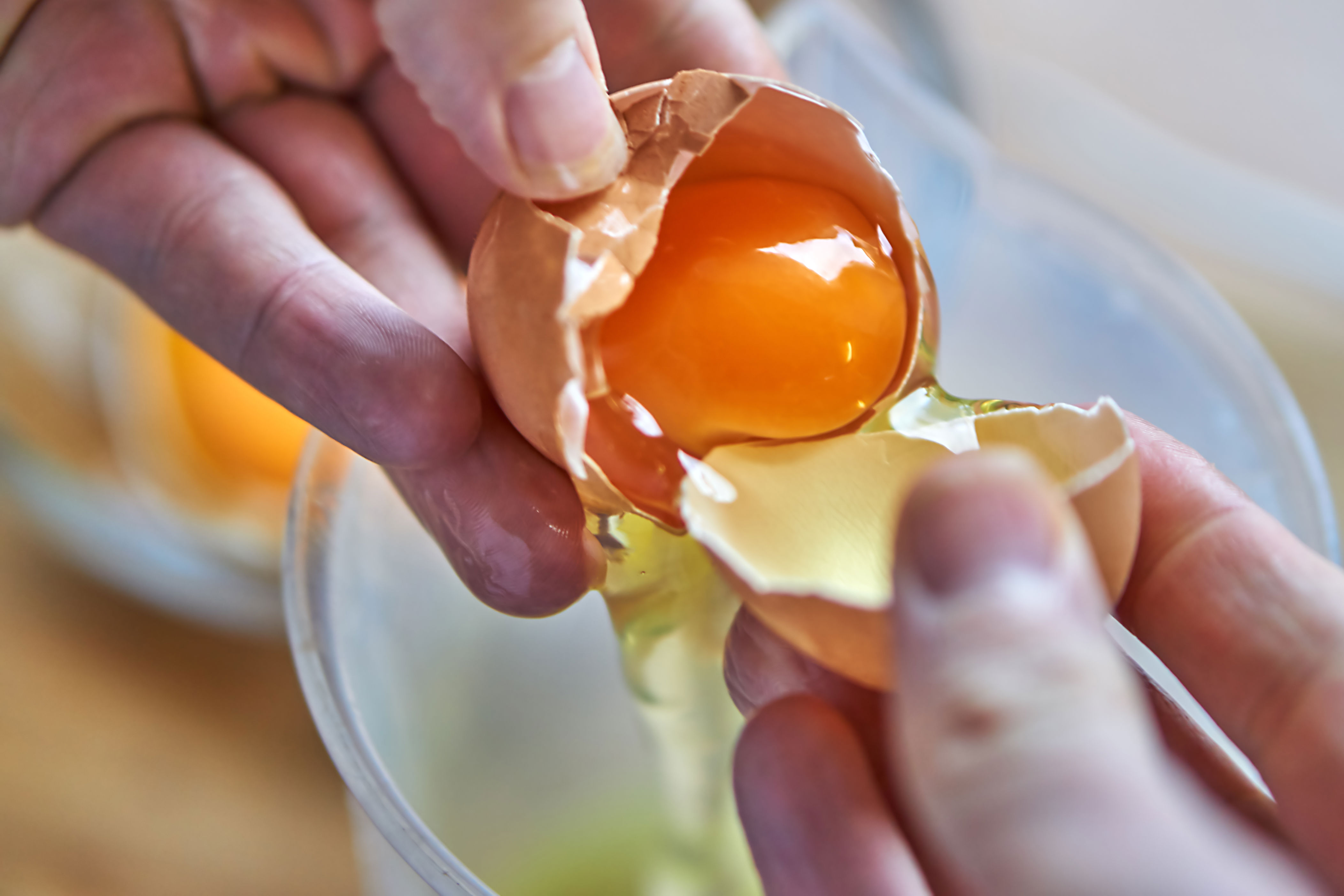A person cracks an egg, letting the yolk and egg white fall into a bowl below