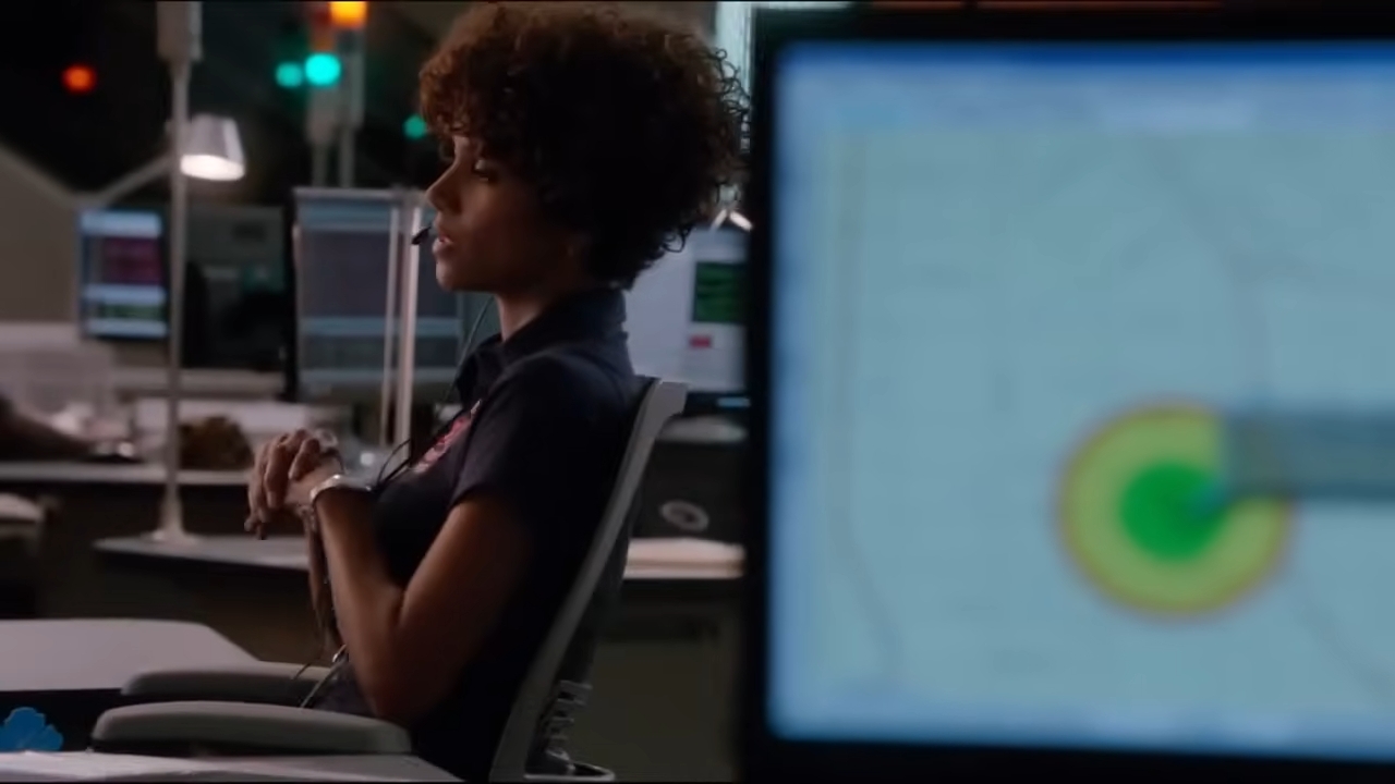 Halle Berry sitting in an office environment, focused on a distant screen in "The Call". In the foreground, a blurred monitor displays a map with a highlighted area