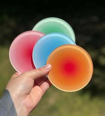 A hand holds four round coasters