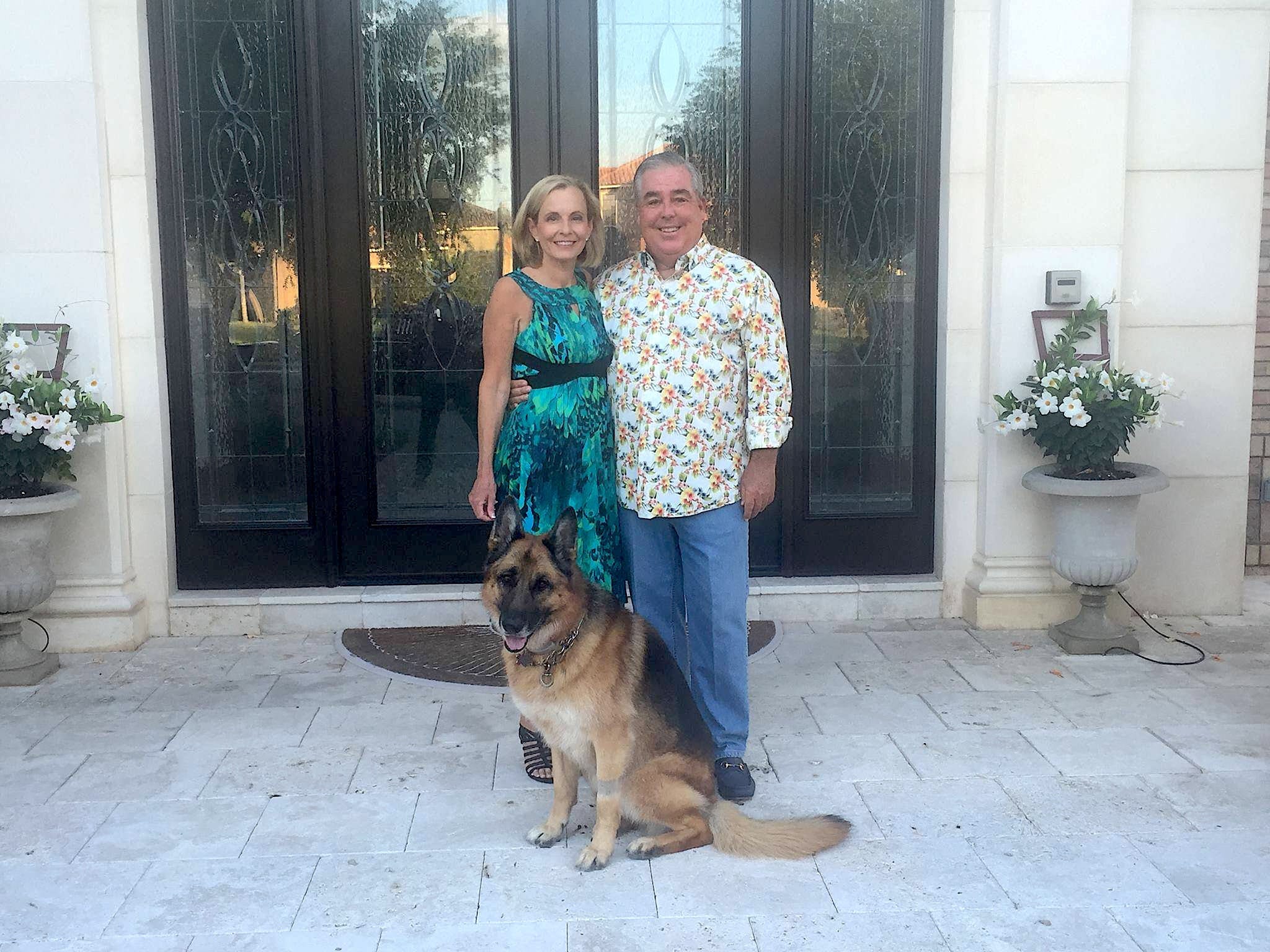 John Morgan and wife standing close with German Shepherd in foreground.