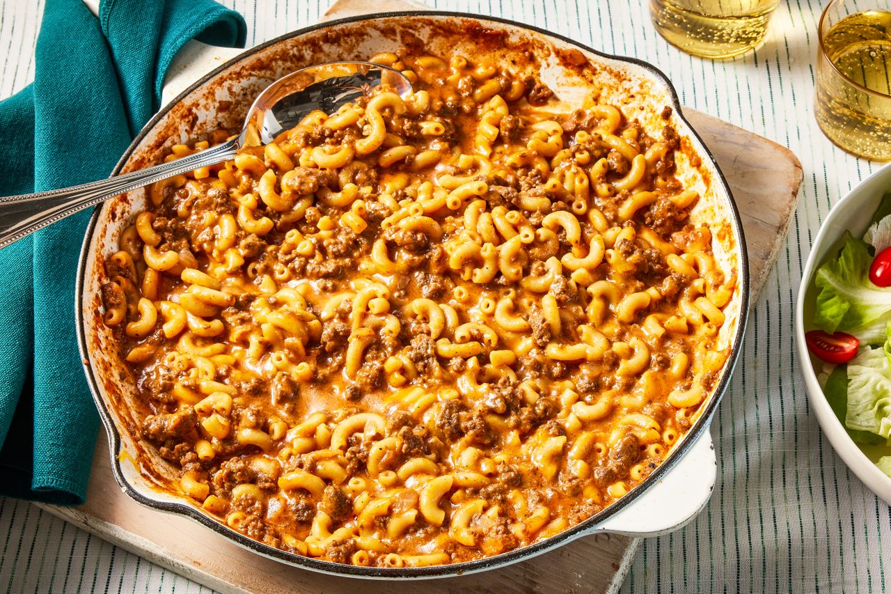 homemade hamburger helper in a skillet at a table setting with two glasses of soda and a side salad