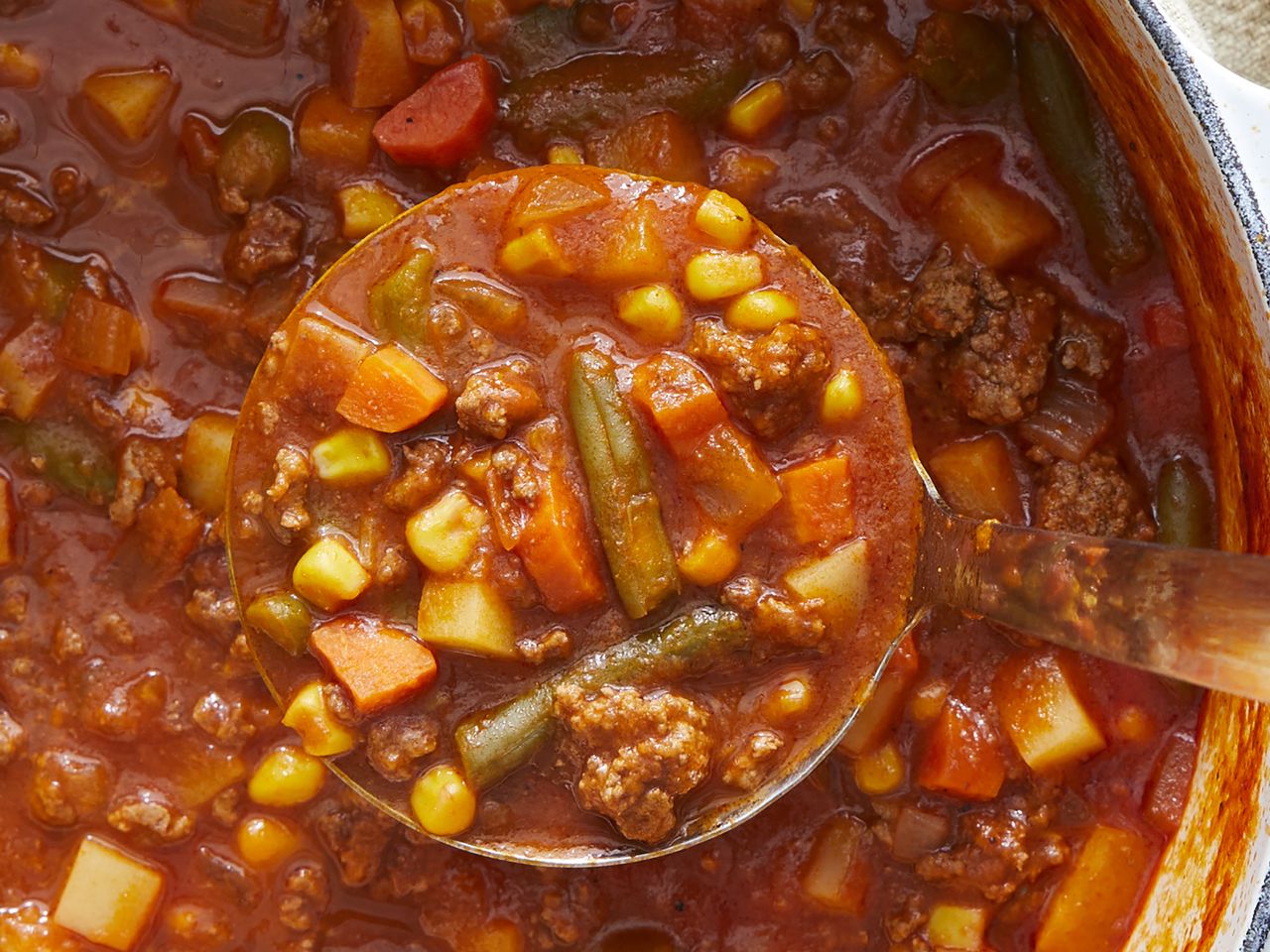 overhead angle looking down at a large spoonful of vegetable soup with a stock pot full underneath