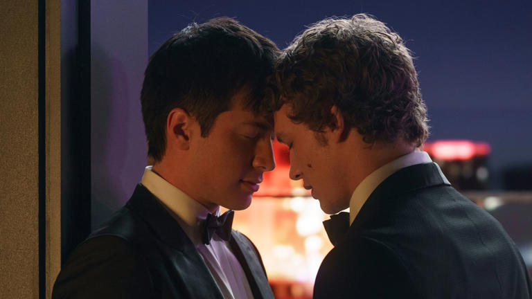 Hudson Williams and Connor Storrie in suits with their heads together in Heated Rivalry