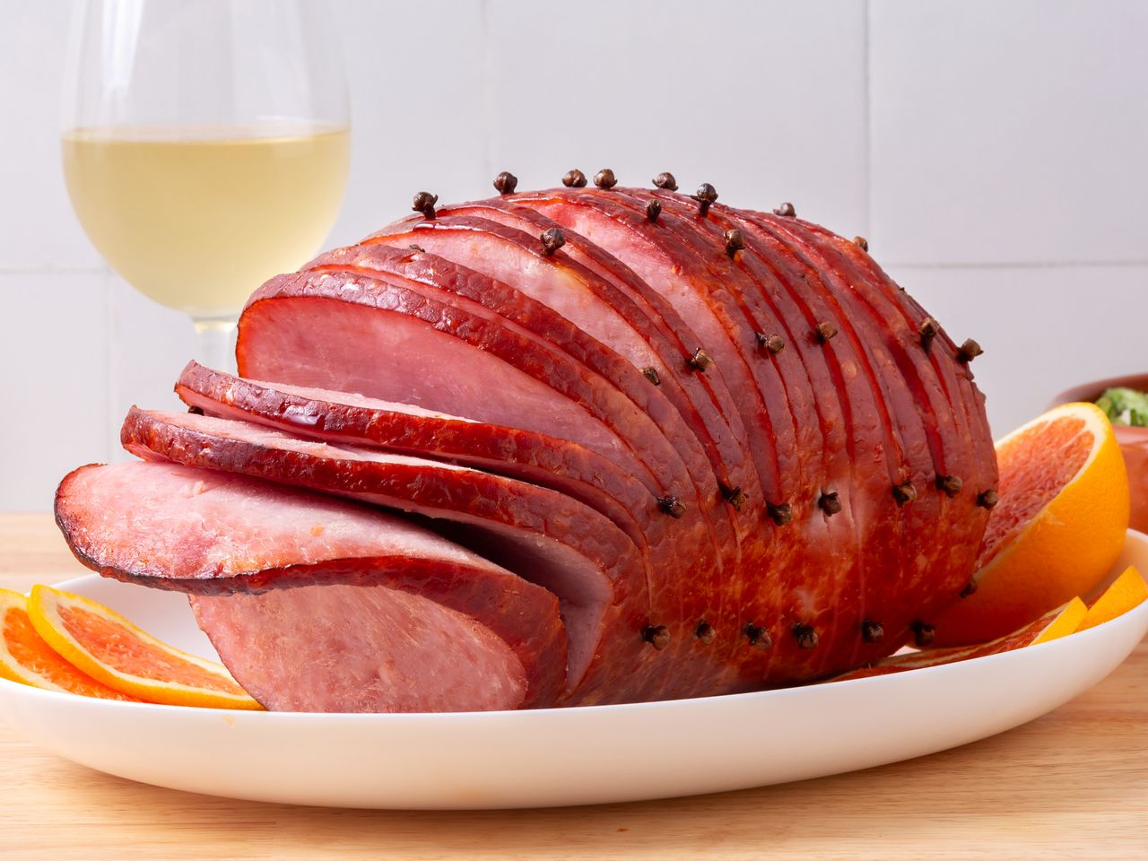 A platter of sliced ham with honey and brown sugar glaze, served with fresh orange slices