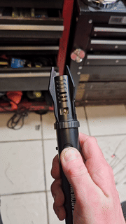 Hand holding a butane torch in a workshop setting, demonstrating its adjustable flame