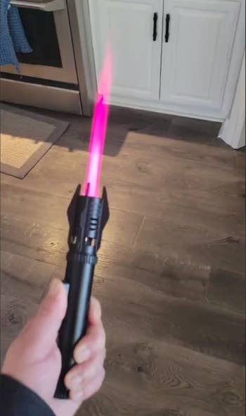 Hand holding a toy lightsaber with a glowing blade in a kitchen setting