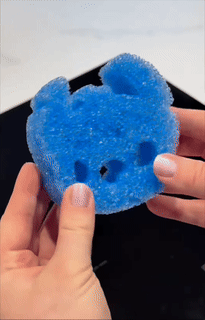 Hands hold a blue scrub sponge shaped like stitch