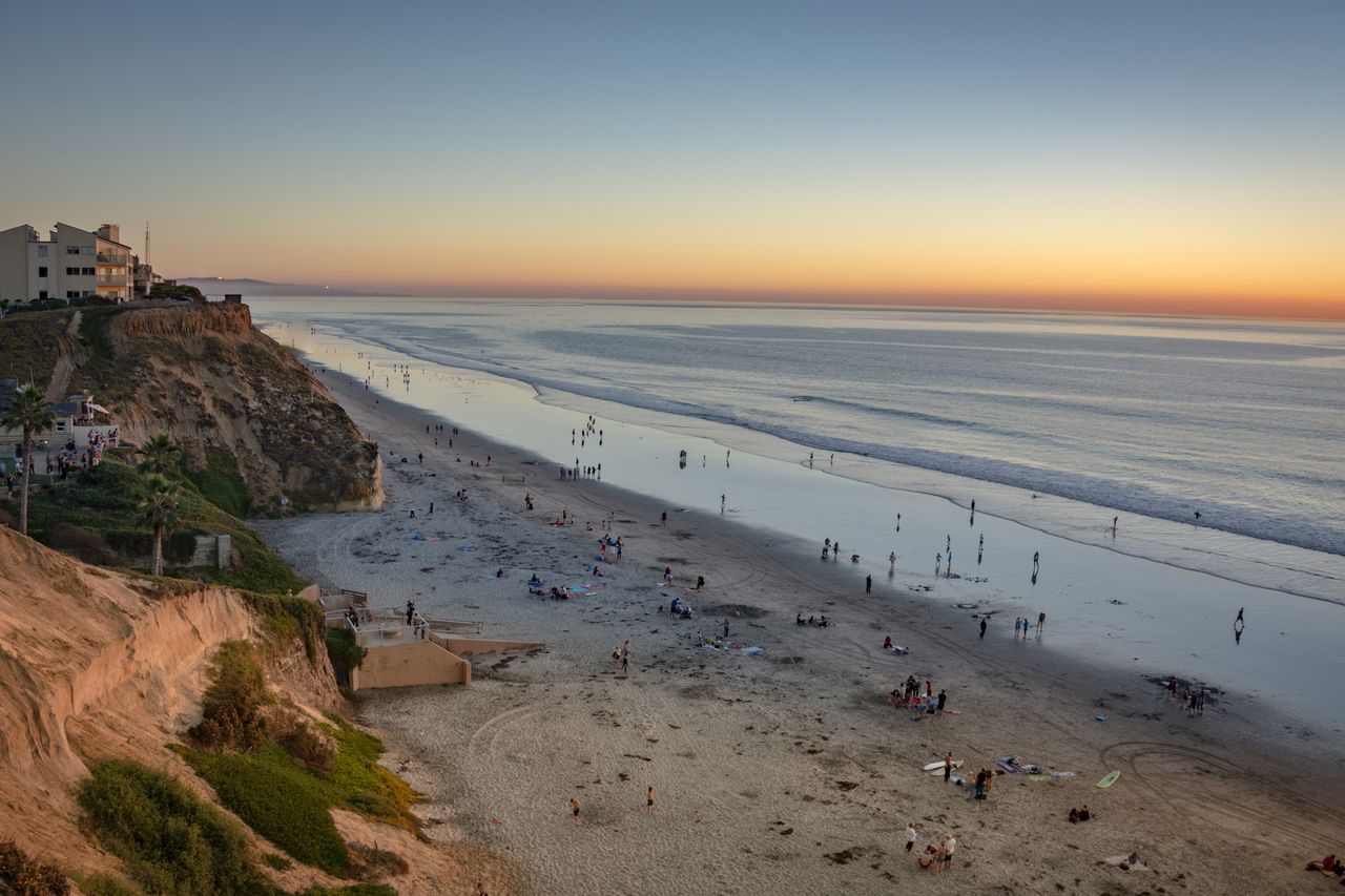 Beach with cliffs buildings and scattered people at sunset