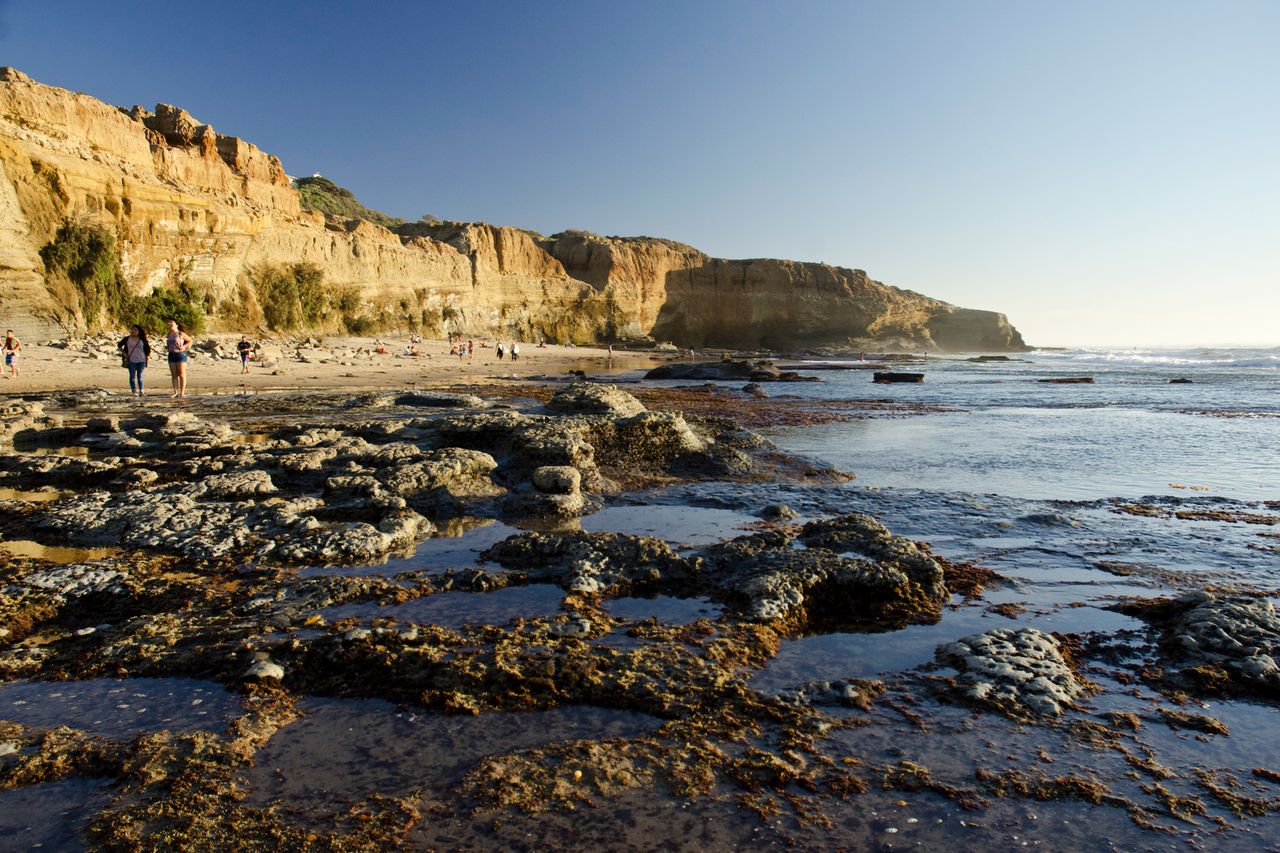 A coastal scene with cliffs tidal rock formations and people walking along the beach